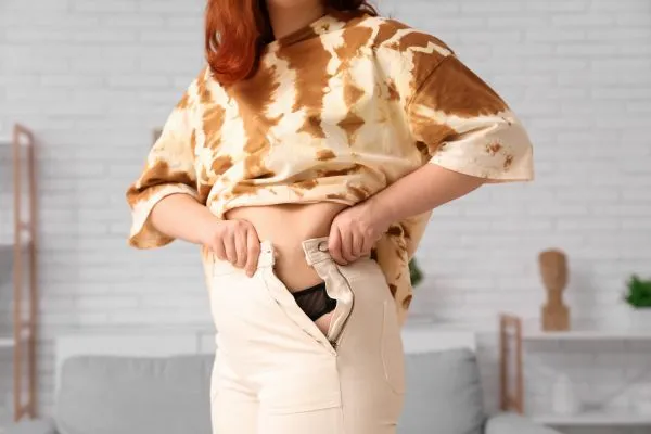 Image of woman trying to do her trousers up after pregnancy weight gain Melksham