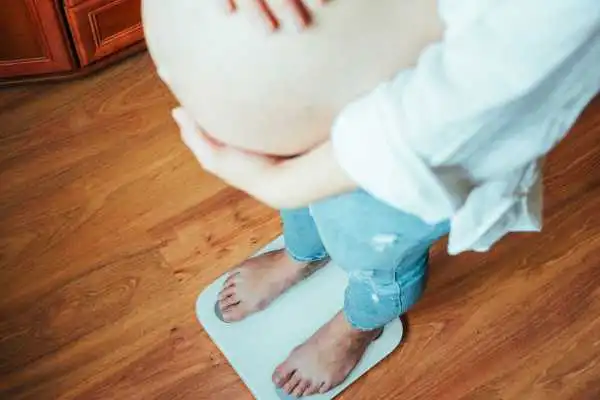 Image of woman weighing herself and experiencing weight gain through pregnancy Melksham